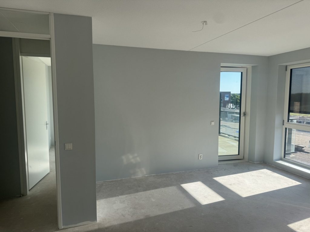 Lege kamer in een nieuw appartement met kale wanden, een betonvloer en een balkondeur