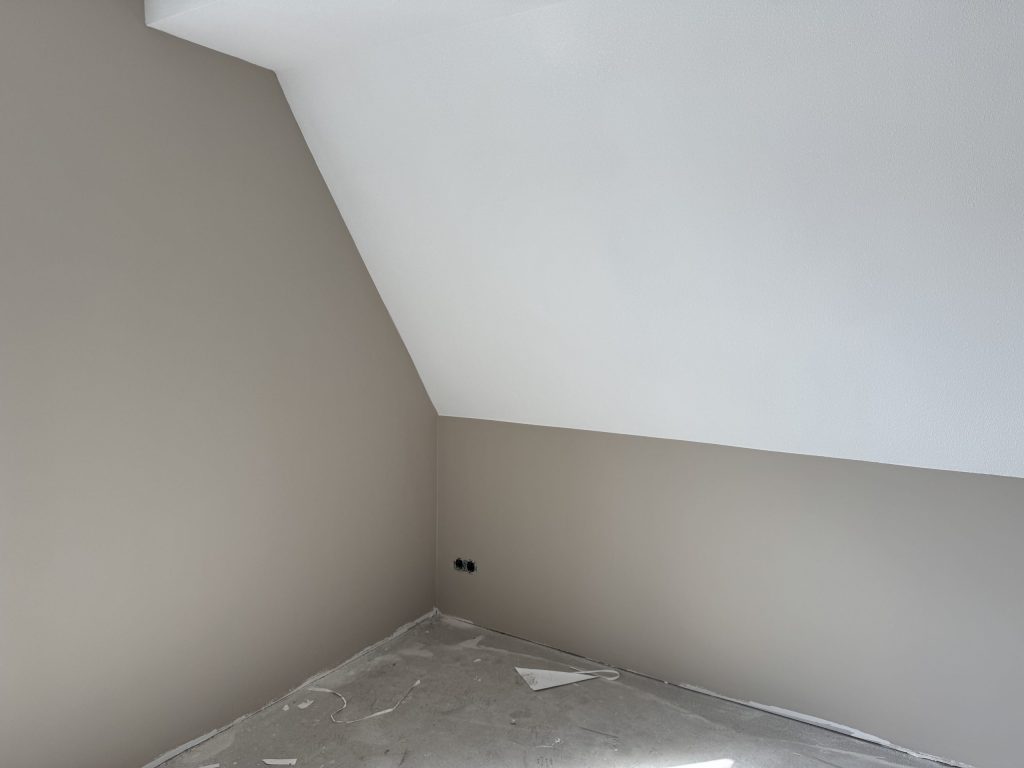 Zolderkamer in een nieuwbouwwoning met een schuine wand en kale muren die klaar zijn voor de afwerking