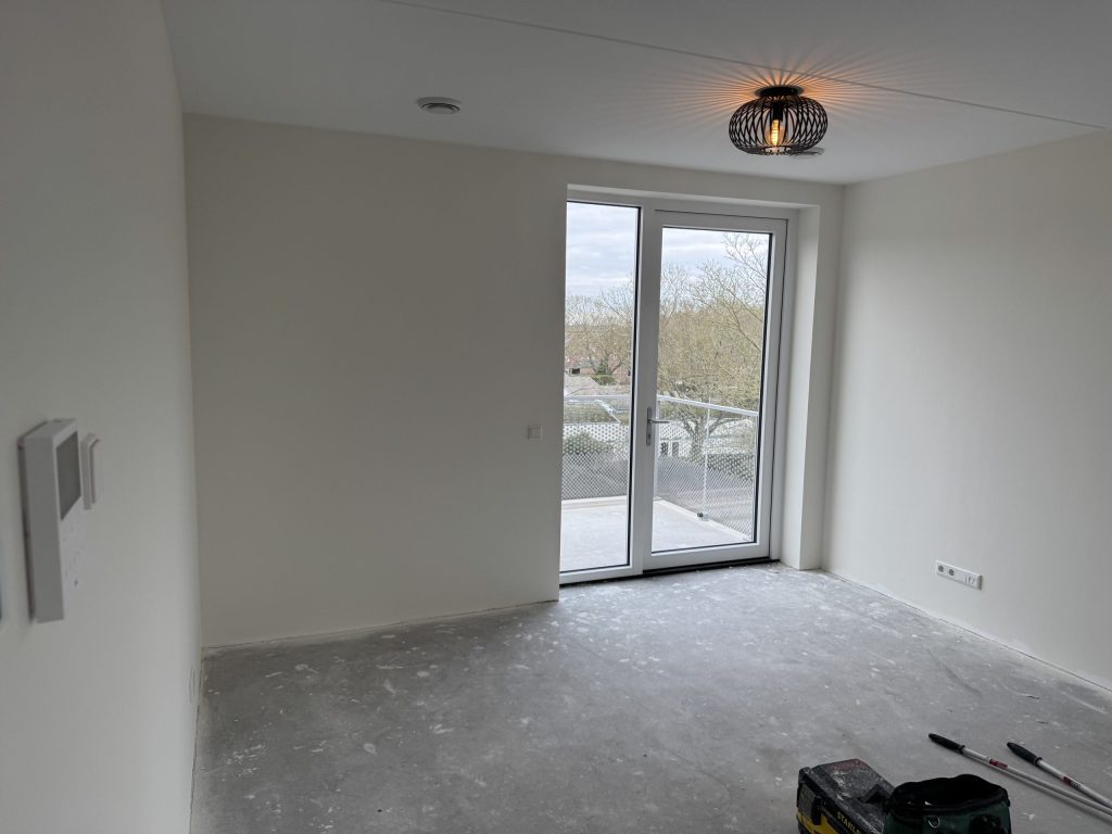 Kamer in een nieuw appartement met witte wanden en openslaande deuren naar het balkon, vlak na de oplevering