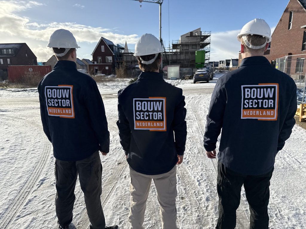 Drie vakmensen met witte helm en bedrijfsjas op een besneeuwde bouwplaats